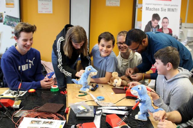 Spielzeuge, Lötkolben, Schleifpapier und viele weitere Materialien liegen auf dem Werktisch. Ringsherum sitzen Schüler und lachen. Zwei davon sind über den Spielzeugen gebeugt und scheinen sich daran zu schaffen zu machen. Vielleicht hat der Affe wieder gefurzt?! Da bleibt kein Auge trocken. Außer man hat keinen Humor. So wie der alte Witz: Sagt der Arzt: "Wir haben ihnen ihren Sinn für Humor herausoperiert!" Sagt der Patient: "Kann ich nicht drüber lachen!"