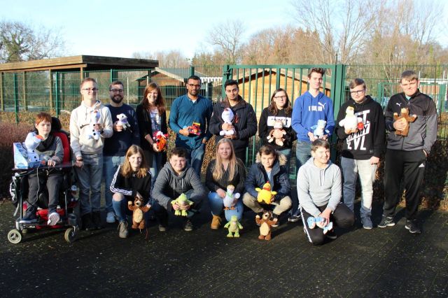 Gruppenbild: Die SchülerInnen und Erwachsenen halten Spielzeuge und blinzeln schön aufgereiht in die Kamera.