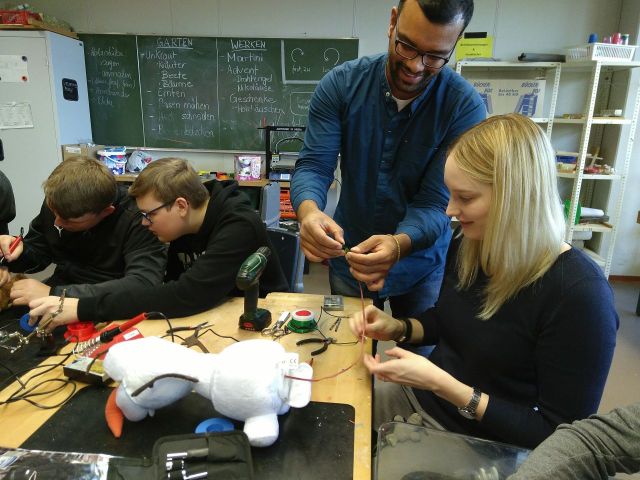Ein Mann und eine junge Frau inspizieren ein Kabelende, das aus einem Spielzeug-Schneemann heraus kommt (Olaf).